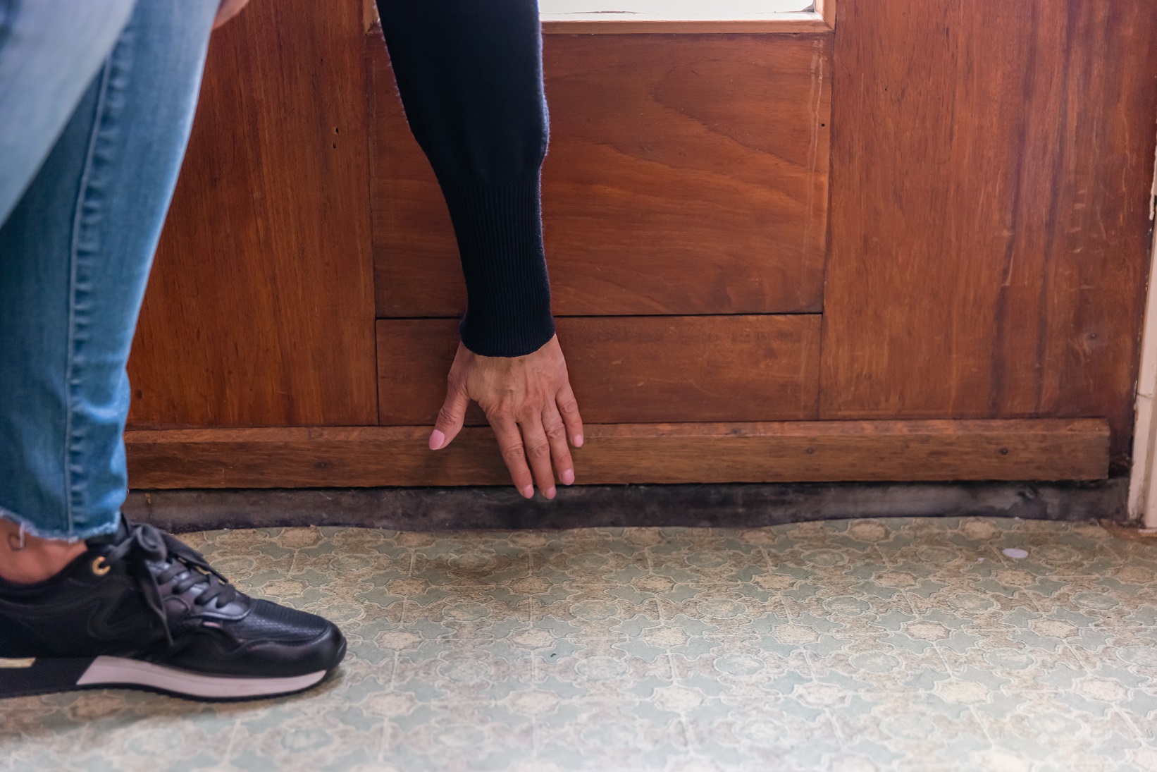 Vrouw voelt met haar hand of er tocht onder de deur vandaan komt.