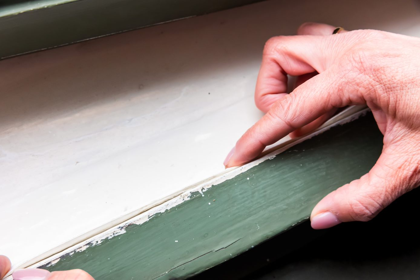 Iemand controleert de tochtband in de kier tussen de sponning en het raam.