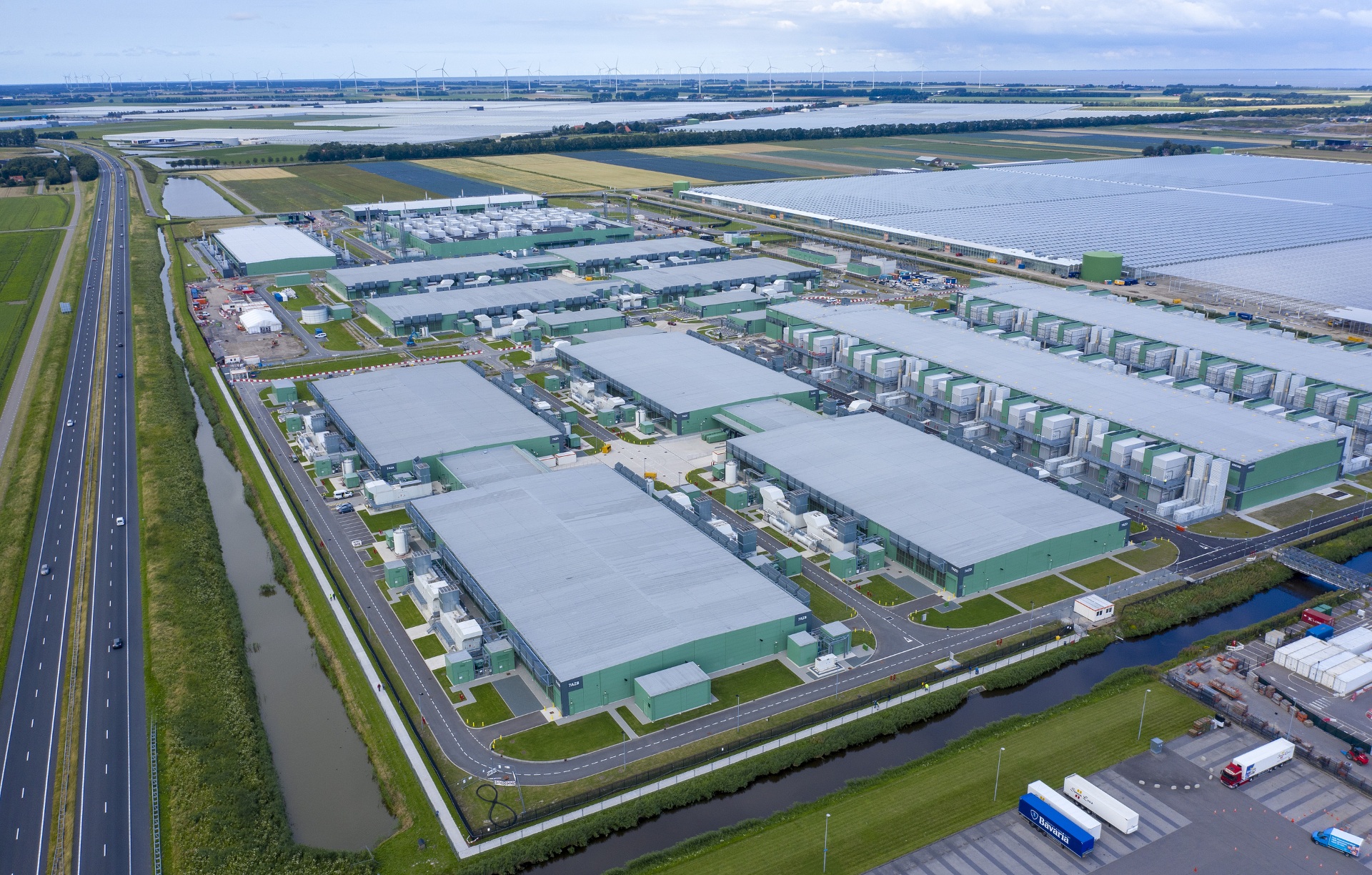 Luchtfoto van een groot, hyperscale datacenter in Middenmeer. Naast het datacenter loopt de snelweg en ligt een veld met zonnepanelen.